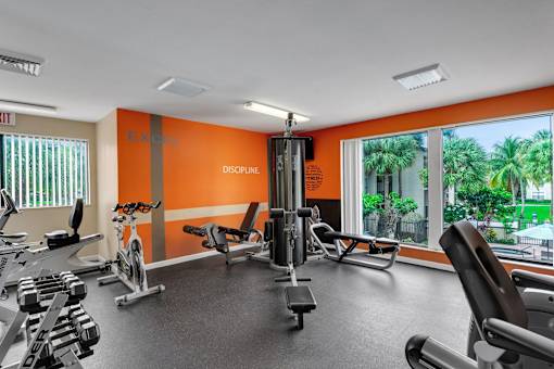 A gym with orange walls and a variety of equipment at Boca Colony Apartments, Boca Raton