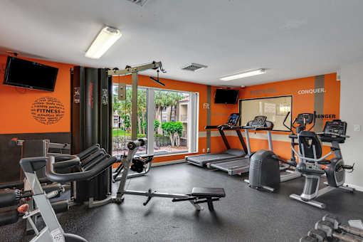 A gym with orange walls and a variety of equipment at Boca Colony Apartments, Florida