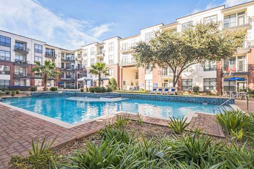 A swimming pool surrounded by a brick border and palm trees in front of apartment buildings  at The Atlantic Memorial, Houston