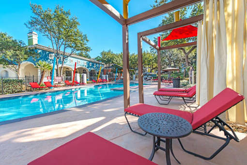 A pool area with red lounge chairs and a table at Reserve at Canyon Creek,Texas