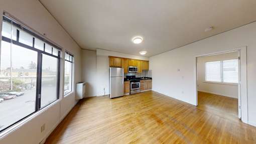 A large empty room with wooden floors and a kitchen area in the background.