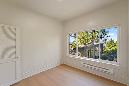 A room with a window showing a view of trees and a house.