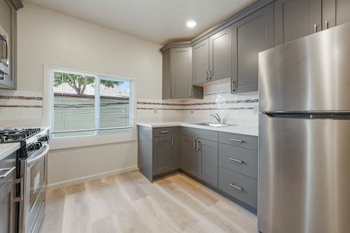A modern kitchen with a stainless steel refrigerator and wooden flooring.