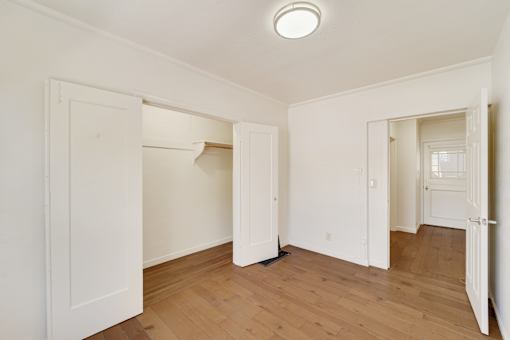 A room with white walls and wooden floors with a doorway open to another room.