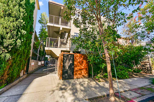 A tree stands in front of a building with a gate.