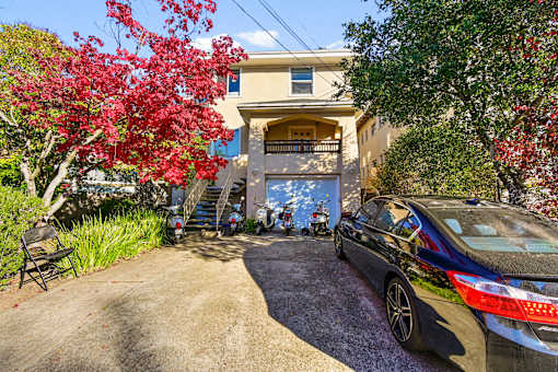 A car is parked in front of a house with a tree with red leaves.