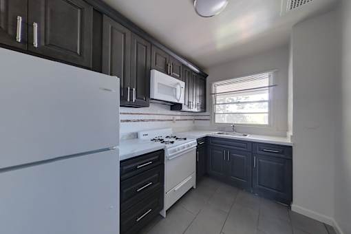 A kitchen with a white fridge, black cabinets, and a window.
