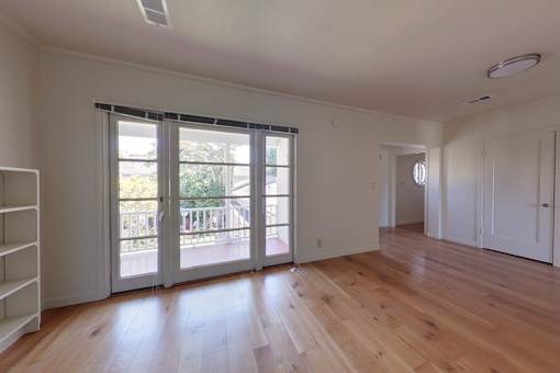 A room with wooden floors and a large window with a view of a balcony.
