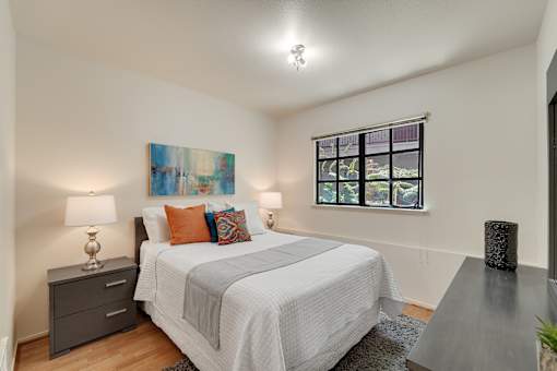 A bedroom with a bed, nightstand, and a painting on the wall.