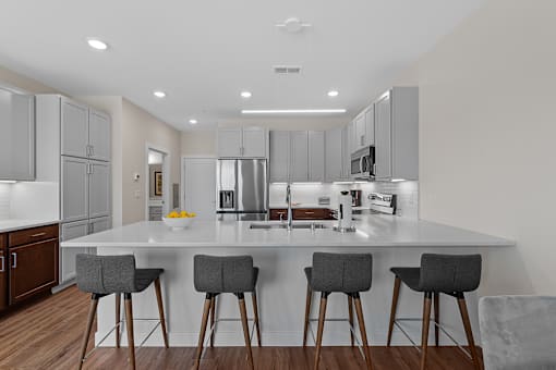 A modern kitchen with a white island and grey bar stools  at Tivoli Green Apartments & Townhomes, Mount Pleasant, 53406