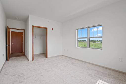 A room with a carpeted floor, a window, and two doors.