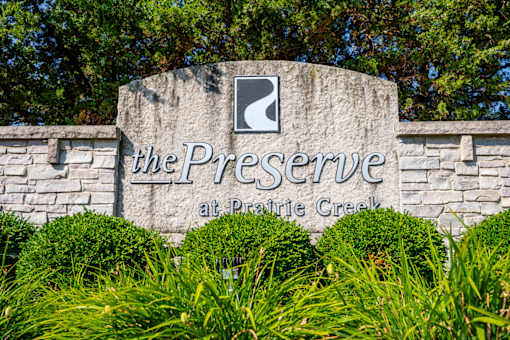 A sign that says "The Preserve at Prairie Creek" is surrounded by green bushes.