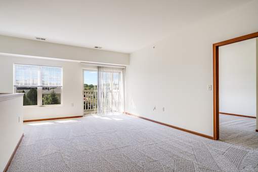 A large, empty room with a carpeted floor and a sliding glass door leading to a balcony.