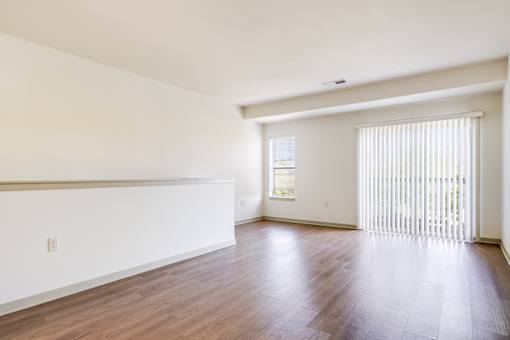 A large empty room with wooden floors and a window with blinds.