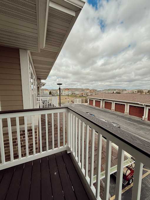 A balcony with a white railing and a view of a parking lot and other buildings.