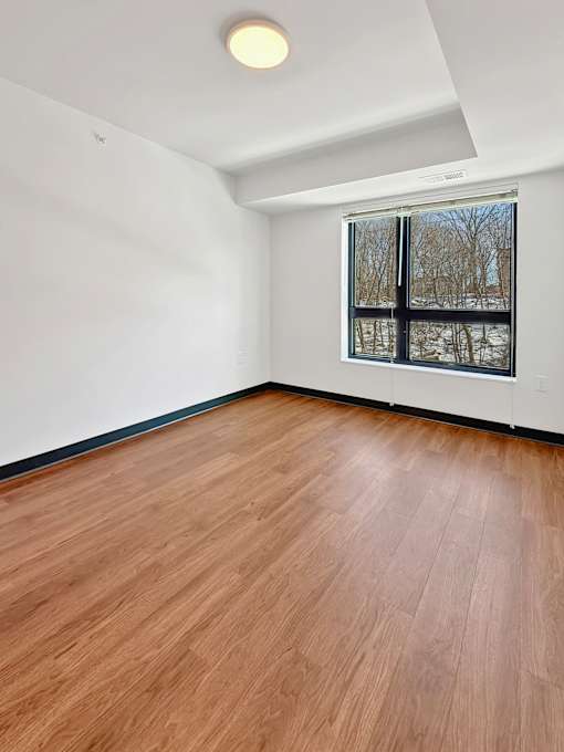 A Stryker Senior Apartments in West St. Paul bedroom with a window and wooden flooring.