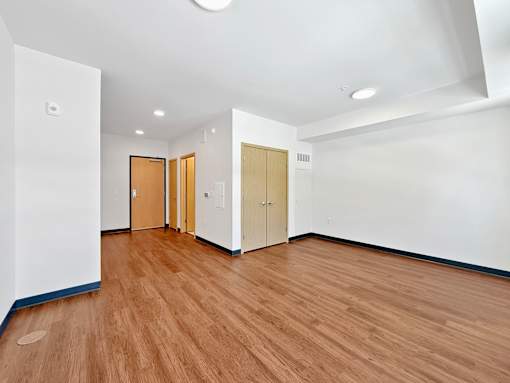 A studio apartment living room at Stryker Senior Apartments in West St. Paul  with wooden floors and white walls with three doors.