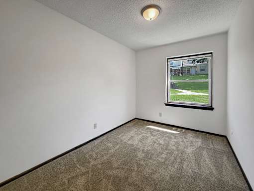 A room with a carpeted floor and a window showing a view of a building and trees.