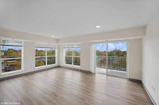 A spacious room with wooden floors and large windows overlooking a balcony.