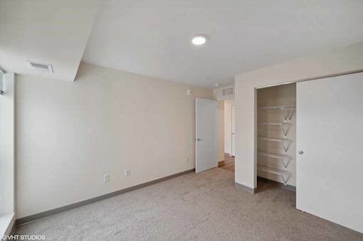 A spacious room with a carpeted floor and a closet with drawers.