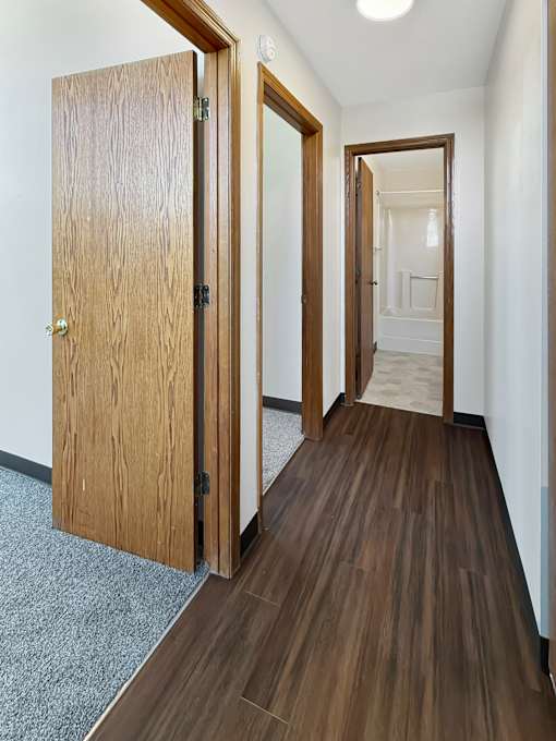 A hallway with a wooden floor and two open doors.