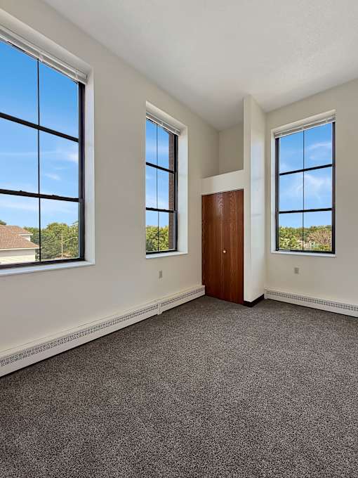A room with a carpeted floor, a brown door, and two windows.