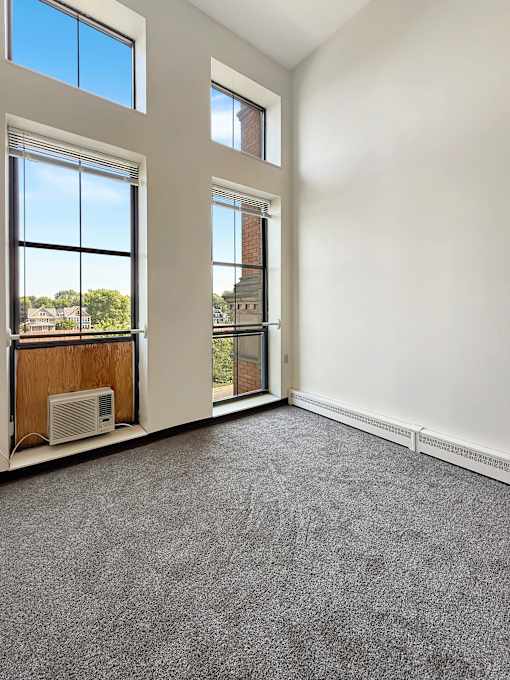 A room with a carpeted floor and two large windows.