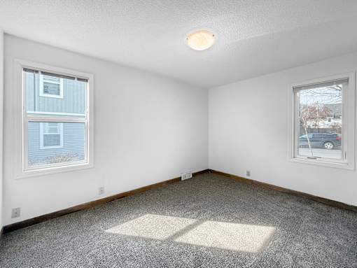 A bedroom room with a carpeted floor, two windows, and a ceiling light.