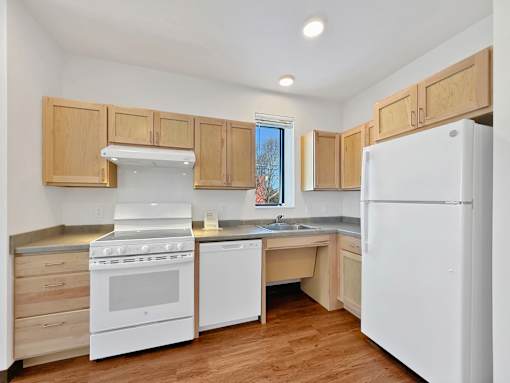 An L shaped kitchen at Stryker Senior Apartments in West St. Paul with white appliances and wooden cabinets.