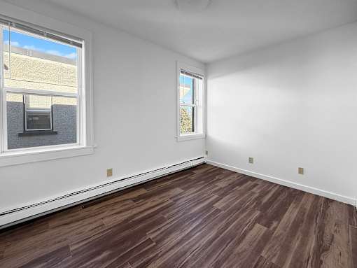 A room with wooden flooring and two windows.