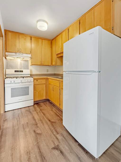 A white refrigerator stands in a kitchen with wooden cabinets.