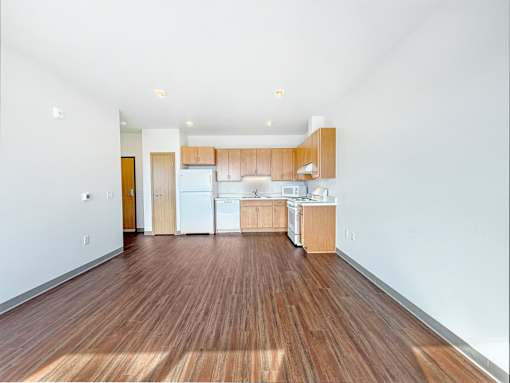 A studio apartment with white appliances and wooden floors.