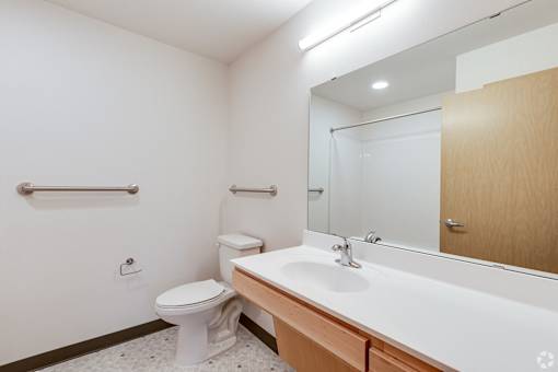 a Stryker Senior Apartments in West St. Paul bathroom with a large mirror and a sink and a toilet