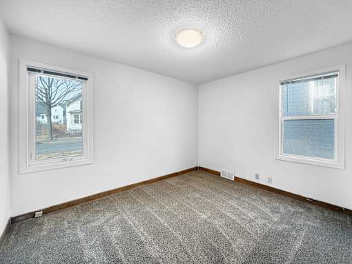 A room with a carpeted floor and two windows.
