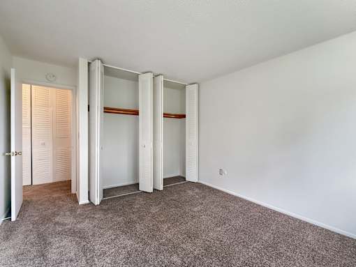 A room with a carpeted floor and a white wall with a door and a wardrobe.
