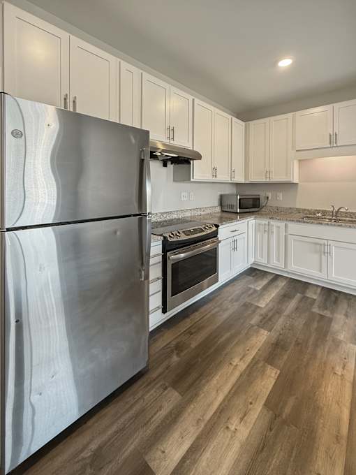 A kitchen with a stainless steel refrigerator and wooden floors.