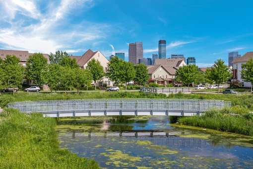 A bridge over a pond with a city skyline in the background.