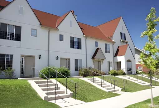 A white building with red roofs and a green lawn in front.
