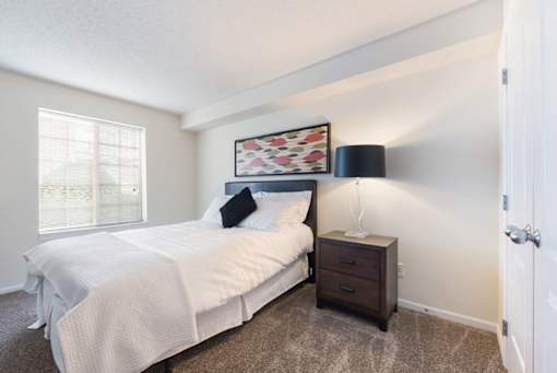 A bedroom with a bed, nightstand, and lamp.
