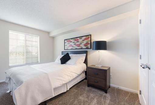 A bedroom with a bed, nightstand, and a window.