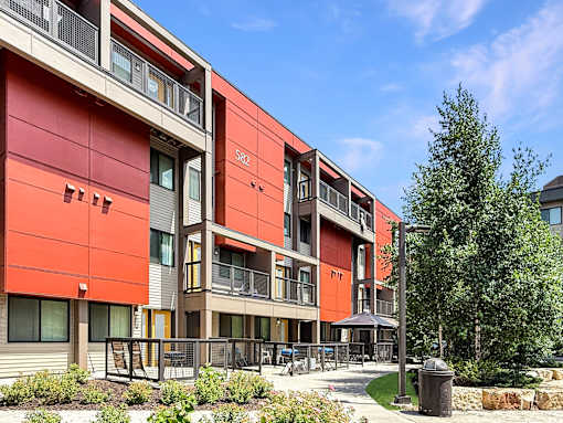 A modern building with a red and beige exterior and a courtyard in front.