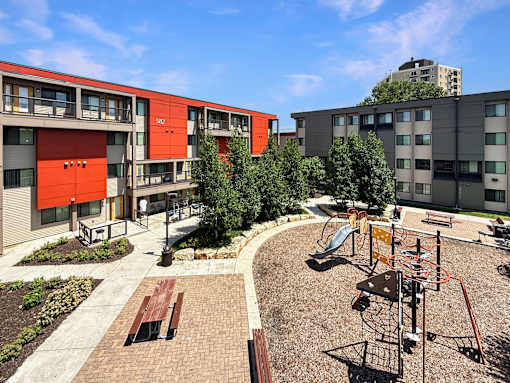 A playground with a slide and a play structure in the foreground and apartment buildings in the background.