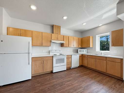 A photo of a kitchen with white appliances and a window