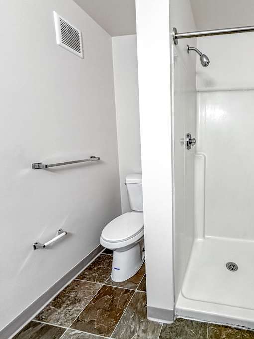 A white toilet with a white shower stall with a silver handle.
