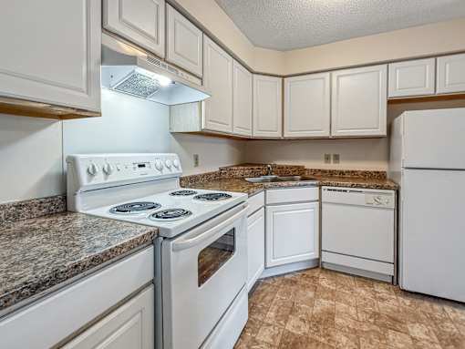 A kitchen with white appliances and brown tiled flooring.