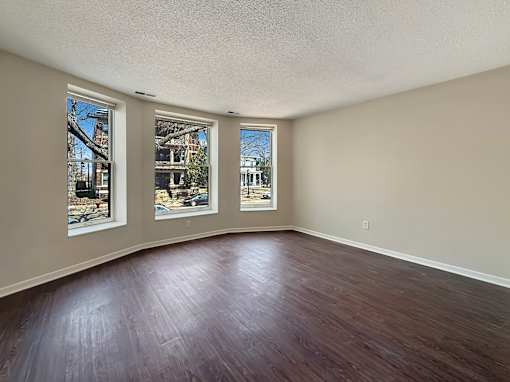 Empty room with wood flooring and three windows.
