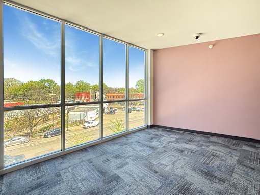 A room with a large window overlooking a parking lot and buildings.