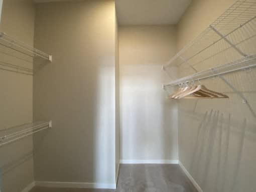 A walk in closet with white shelves and a light shining through the door.