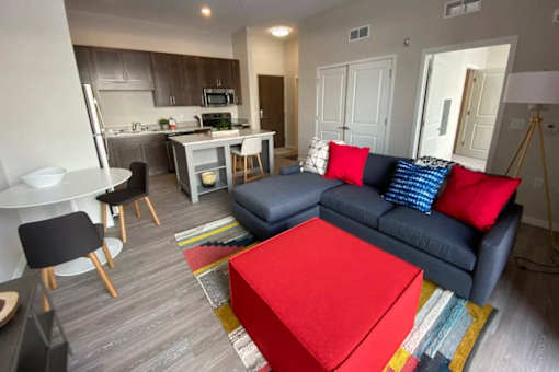A living room with a blue couch and a red ottoman.