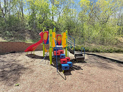 A playground with a red slide, a blue and yellow climbing frame, and a red and blue climbing wall.
